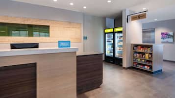 A hotel reception area with a wooden reception desk, a minibar, a cold beverage refrigerator, and a snack shelf.