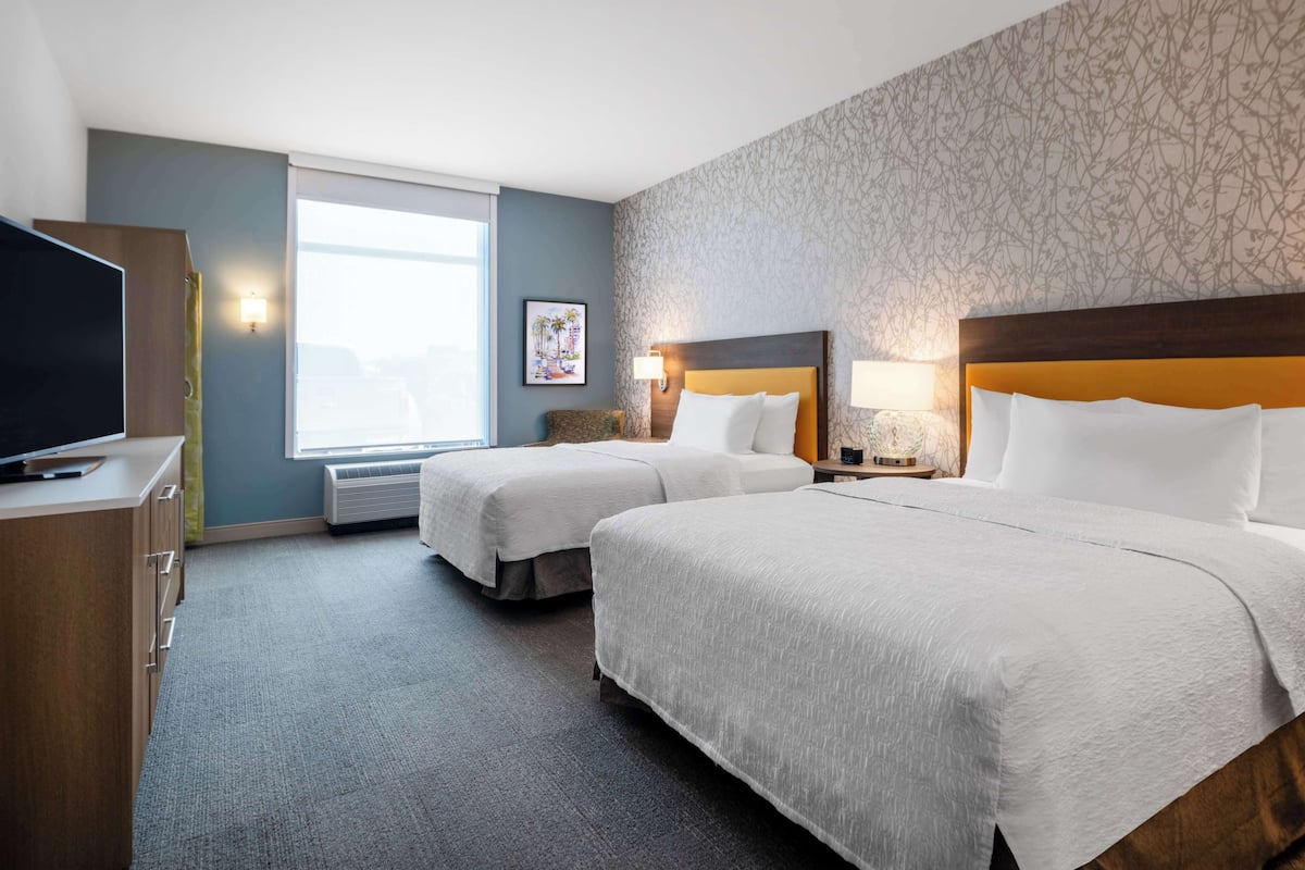 A hotel room with two beds, a TV, a desk, and a window with a view.