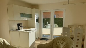Eine kompakte Küche mit Kaffeemaschine, Spüle und integriertem Backofen. Eine Glastür führt zu einem Außenbereich.