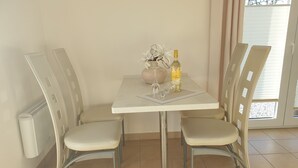 Ein Essbereich mit einem weißen Tisch und vier Stühlen. Auf dem Tisch stehen eine Flasche Alkohol und eine Vase mit Blumen.