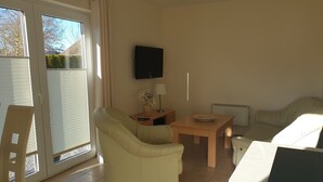 Ein Wohnzimmer mit einer Couch, einem Tisch, einem Fernseher und einer Schiebetür.