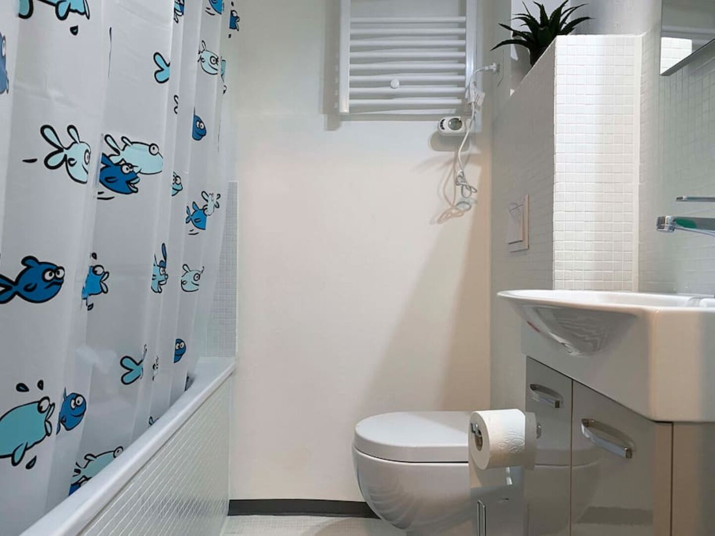 A bathroom with a toilet, a sink, and a shower curtain with cartoon fish designs.