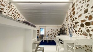 A room with a bunk bed, a desk, and a chair. There is a window with curtains, a plant, and a wall with a stone pattern. - Ca Sistina Blue (Morcote)