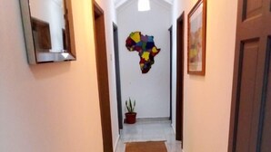 A hallway with a tiled floor, a brown rug, a potted plant, and a colorful map on the wall. - 3 beds 3 bathrooms 5mins from turntable , close to few corner shops and beaches (Brufut)
