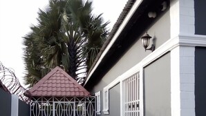 A house with a tiled pathway leading to a gated entrance, a small gazebo, and a large tree in the background. - 3 beds 3 bathrooms 5mins from turntable , close to few corner shops and beaches (Brufut)