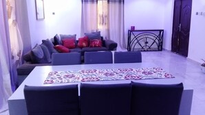 A spacious living room with a sofa set, a dining table with chairs, a ceiling fan, and a decorative metal gate. - 3 beds 3 bathrooms 5mins from turntable , close to few corner shops and beaches (Brufut)