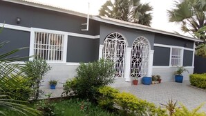 A building with a grey facade, white trim, and large arched windows with white grills. - 3 beds 3 bathrooms 5mins from turntable , close to few corner shops and beaches (Brufut)