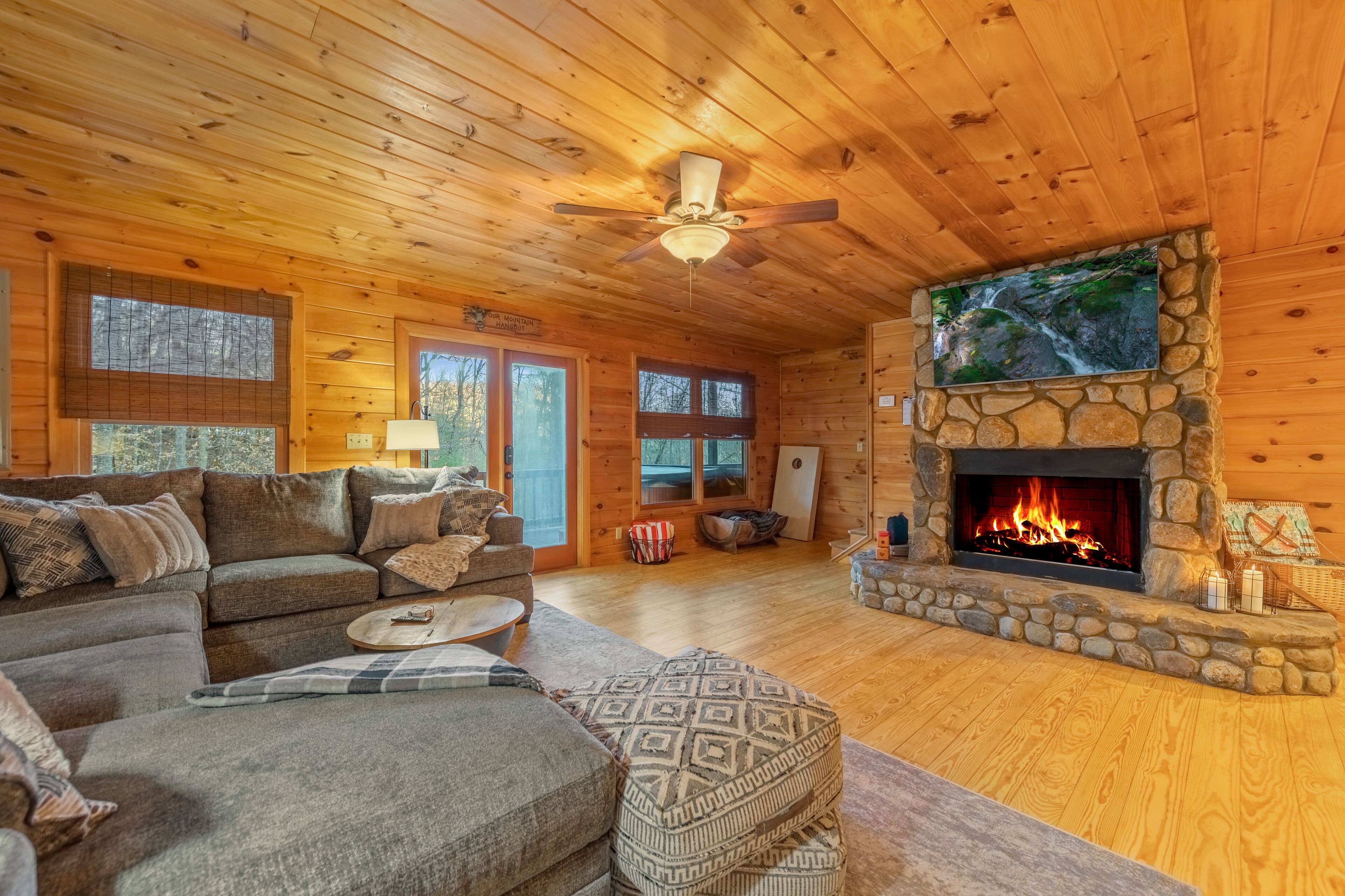 L’intérieur chaleureux d’un chalet avec une cheminée en pierre, un plafond en bois et une grande fenêtre donnant sur une forêt.