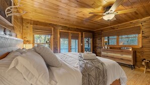 A wooden cabin bedroom with a bed, a dresser, and a ceiling fan.
