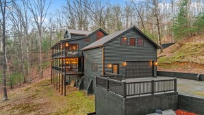A log cabin with a balcony and a garage, surrounded by trees.