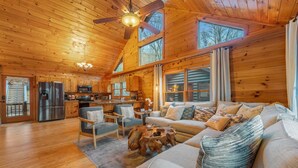 A spacious cabin interior with a wooden interior, a dining area, a living room with a sofa and chairs, and a kitchen with modern appliances.