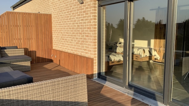 A modern outdoor patio with wicker furniture and a glass sliding door leading to a bedroom.