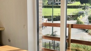 A modern dining area with a large wooden table and metal legs, a clock, and a view of a green landscape through large windows.