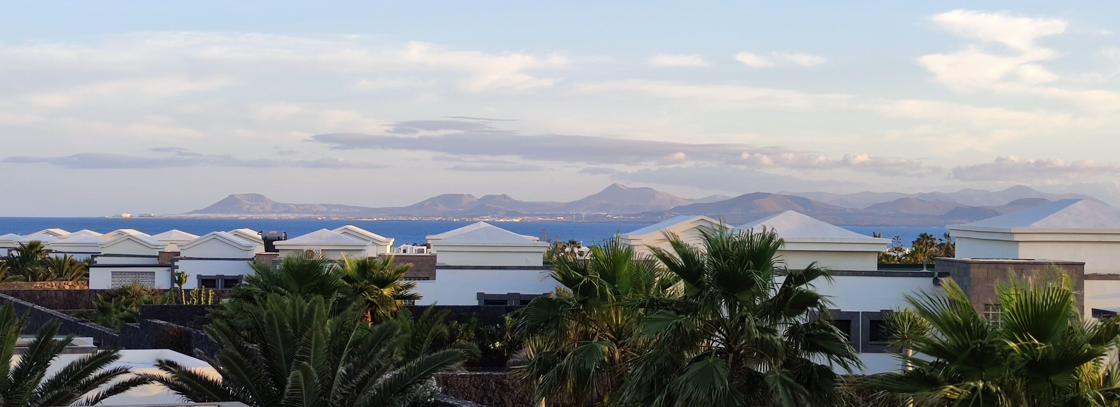 Une station balnéaire dotée de bâtiments modernes aux façades blanches, de palmiers et offrant une vue sur la mer et les montagnes lointaines.