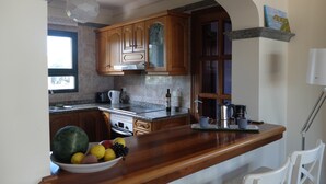 Une cuisine avec des meubles en bois, un plan de travail en marbre et un panier de fruits.
