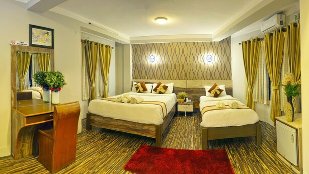 Quarto de hotel com duas camas, uma escrivaninha, um tapete vermelho e um ar-condicionado fixado na parede.