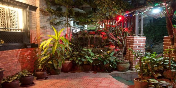 A courtyard with potted plants, a brick wall, and a window with a decorative grille.