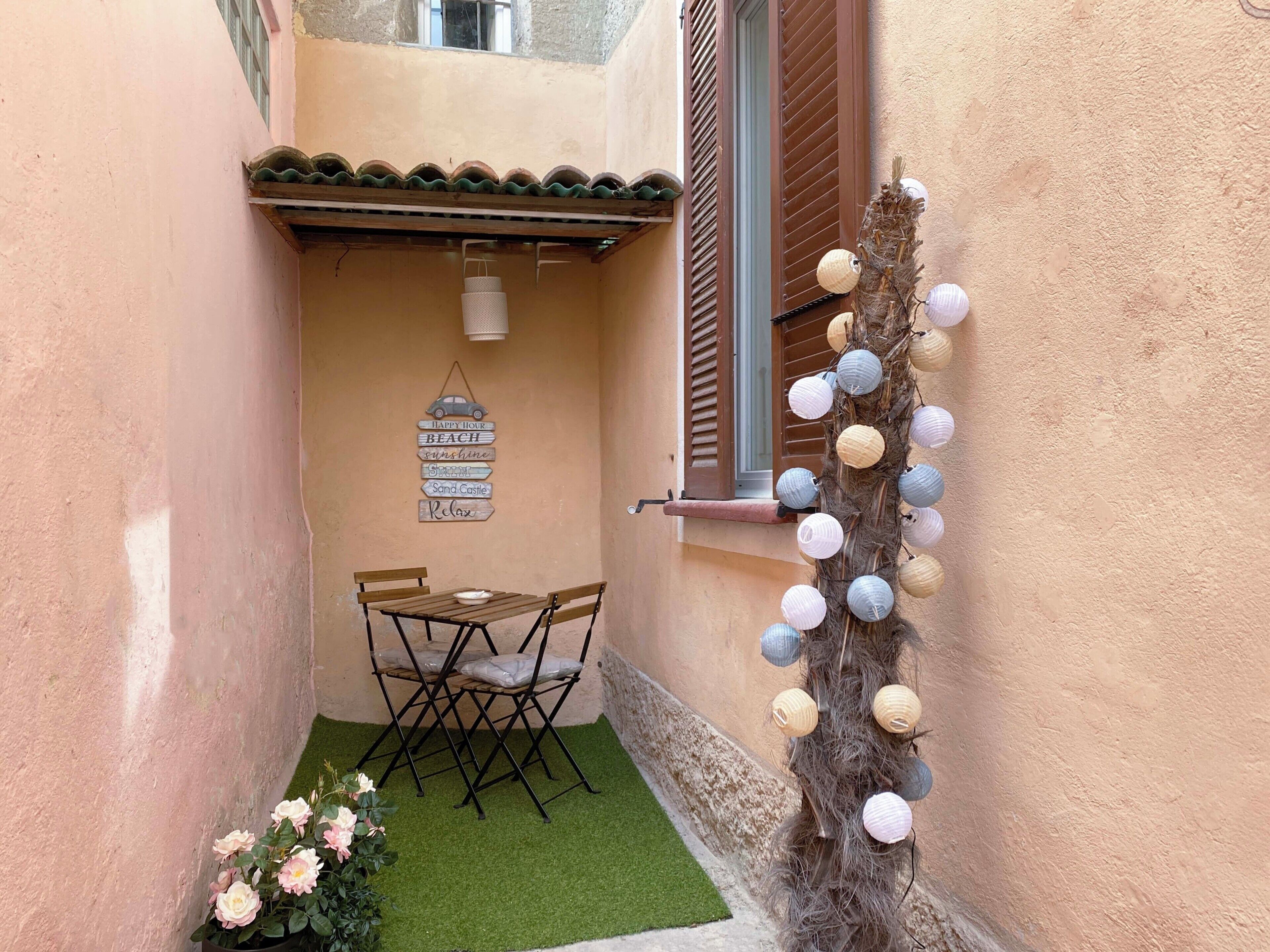 Une petite terrasse avec une table et des chaises, une décoration murale et une guirlande de lanternes en papier.