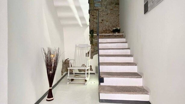 Eine Treppe mit weißen Stufen führt zu einer Zwischenebene. Auf der Zwischenebene stehen ein weißer Stuhl und eine Ziervase.