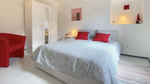 Ein Schlafzimmer mit einem Bett, einem roten Sessel, einem Kleiderschrank und einer Decke mit floralem Muster.