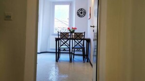 Ein Flur, der in einen Essbereich mit Tisch und Stühlen führt. An der Wand hängt eine Uhr, und auf dem Boden liegt eine rote Fußmatte.