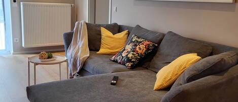 A modern living room with a grey sectional sofa, yellow throw pillows, a small round table with a plant, and a large wall clock.