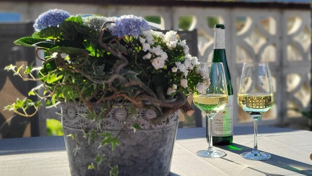 Ein Blumentopf mit Blumen und eine Flasche Weißwein auf einem Tisch im Freien.