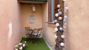 Een klein terras met een tafel en stoelen, een decoratieve muur met een hangend bord en een slinger van papieren lampionnen.