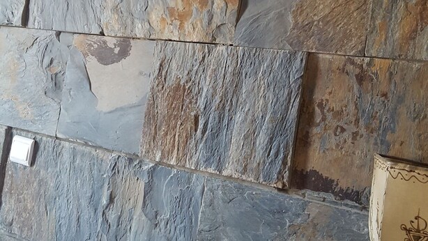 Una habitación con pared de piedra, una cama con ropa de cama blanca y una mesita de noche con una lámpara.