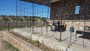 Edificio de piedra con valla metálica, mesas al aire libre y dispensador de agua.