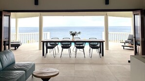 Un espacio abierto que combina sala de estar y comedor, con vistas al mar, una mesa y sillas, y un sofá.