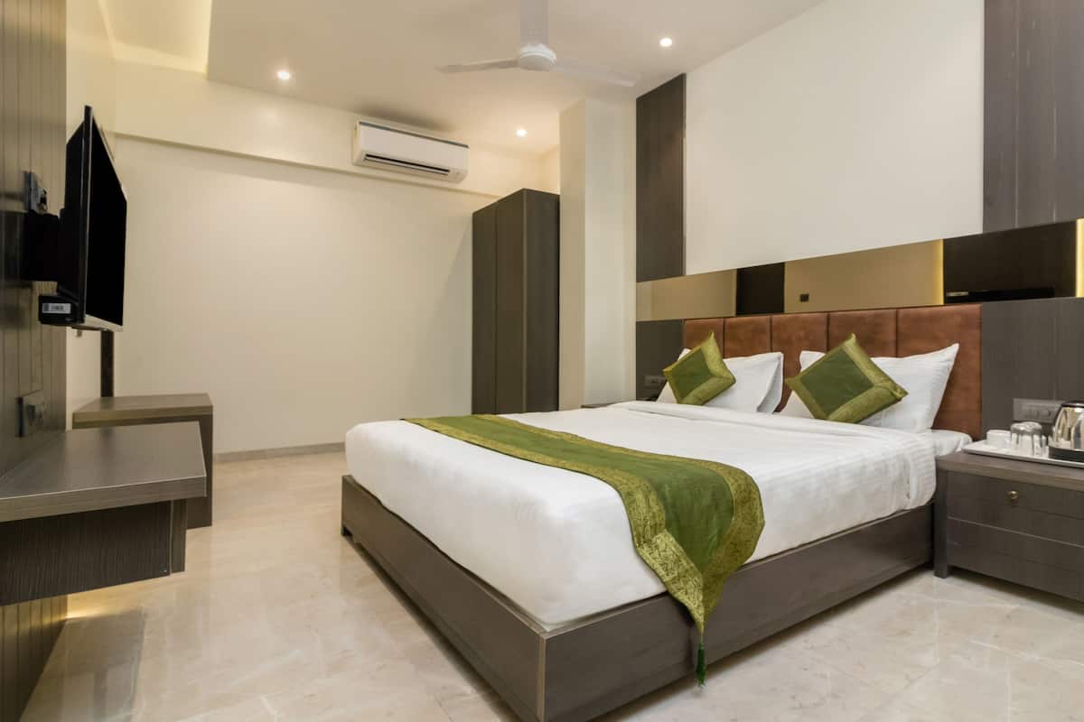 A modern hotel room with a large bed, bedside tables, a wardrobe, an air conditioning unit, and a television.