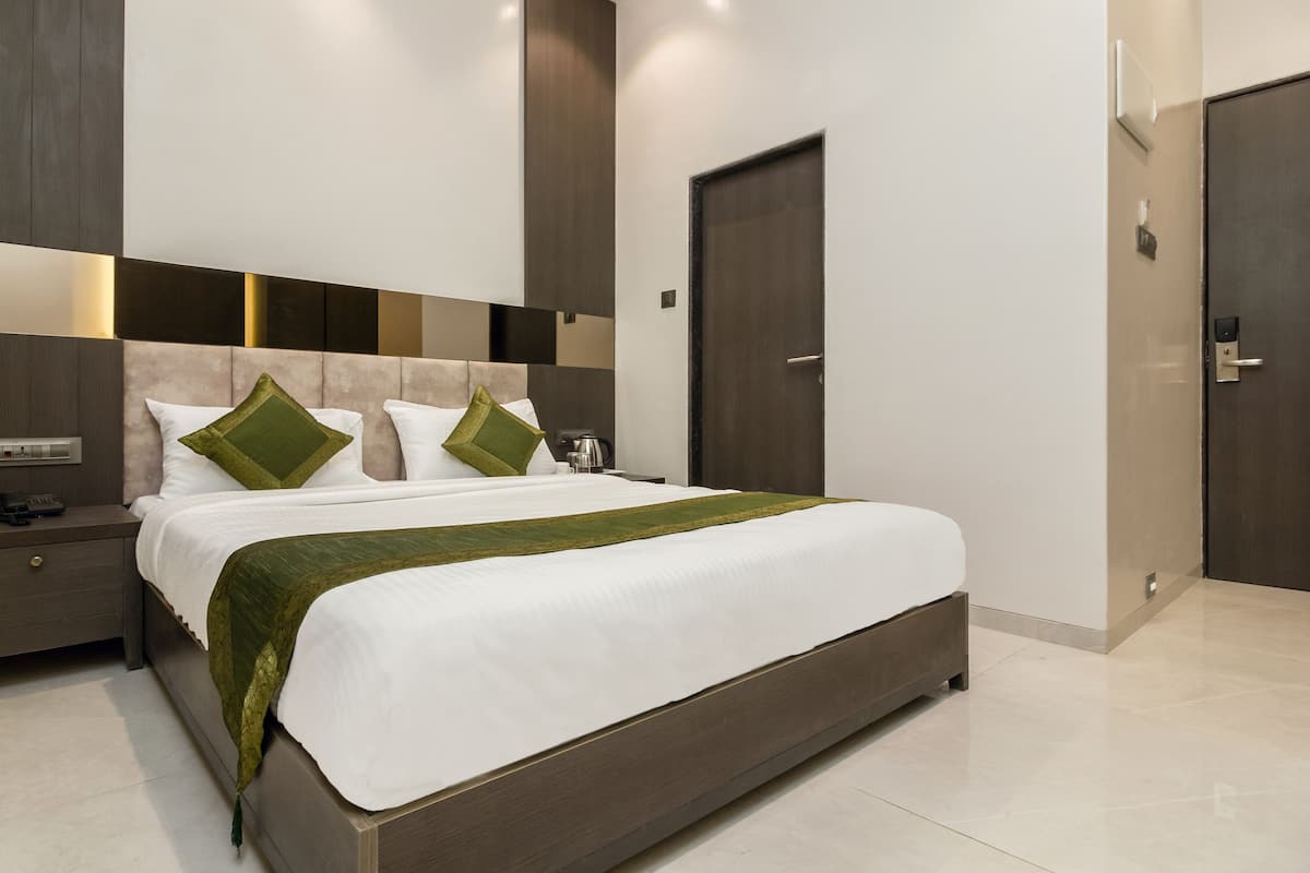 A modern hotel room with a large bed, a nightstand, a bedside table, a wall-mounted light, and a door.