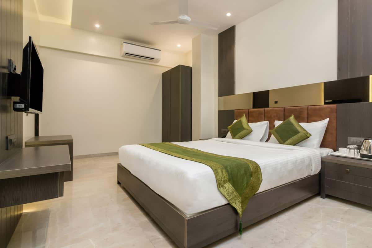 A modern hotel room with a large bed, bedside tables, an air conditioning unit, and a television.