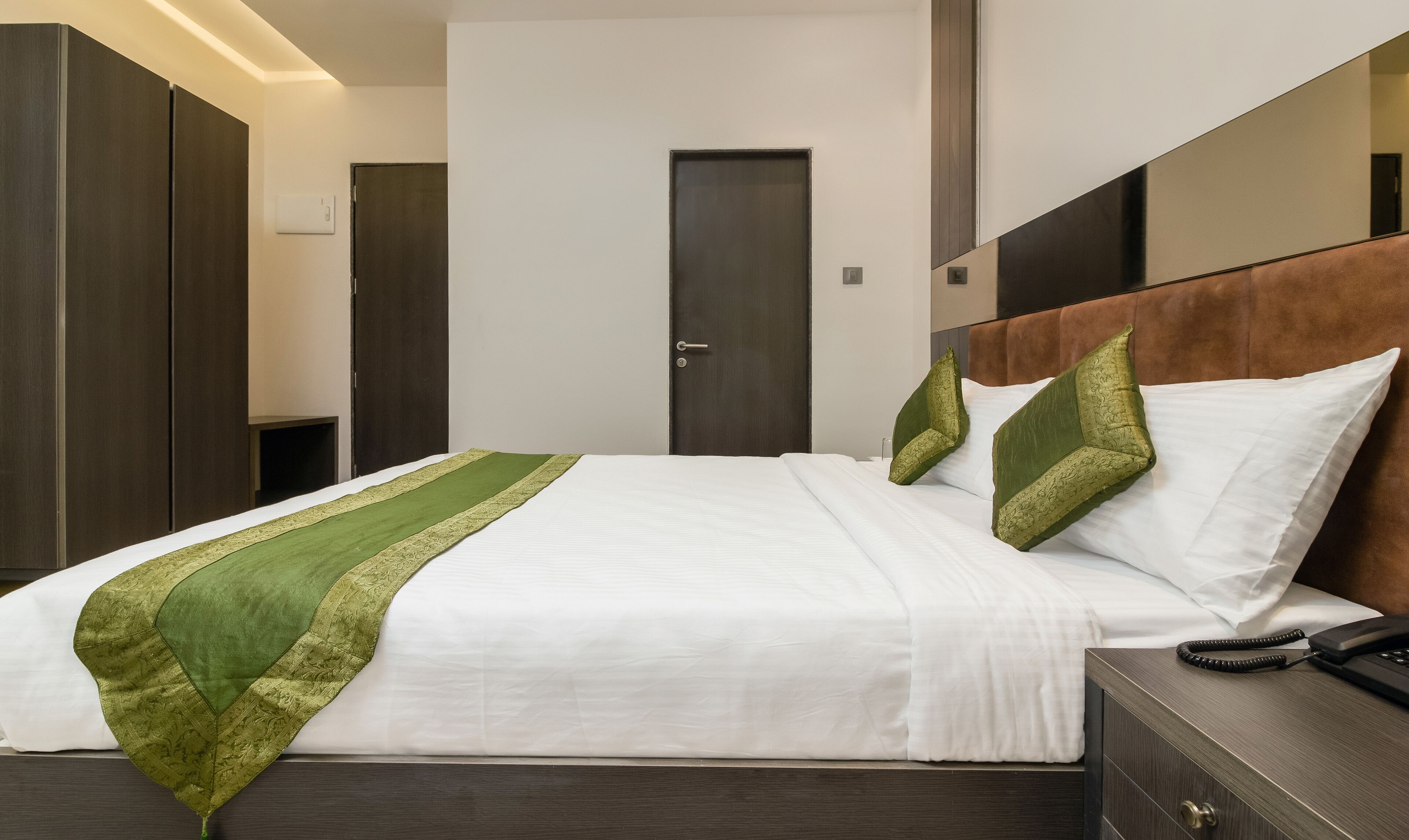 A hotel room with a bed, a bedside table with a telephone, and a door.