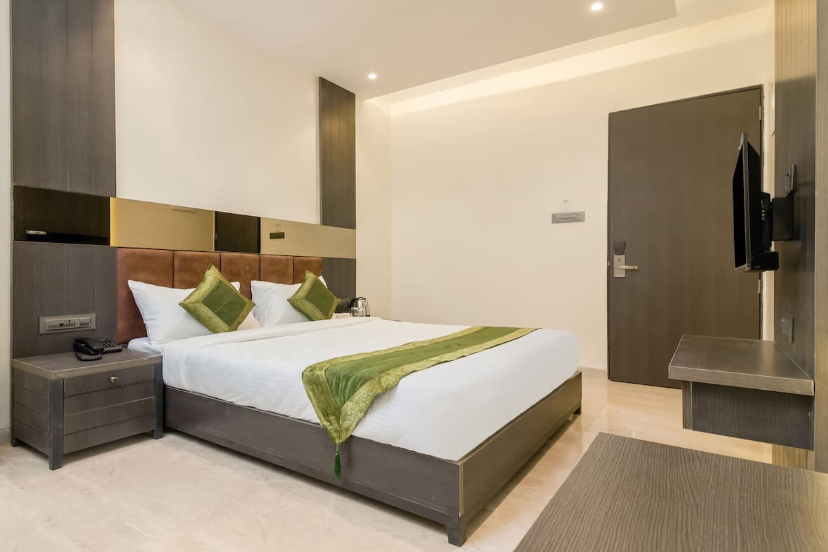 A modern hotel room with a large bed, a bedside table with a phone, and a wall-mounted TV.