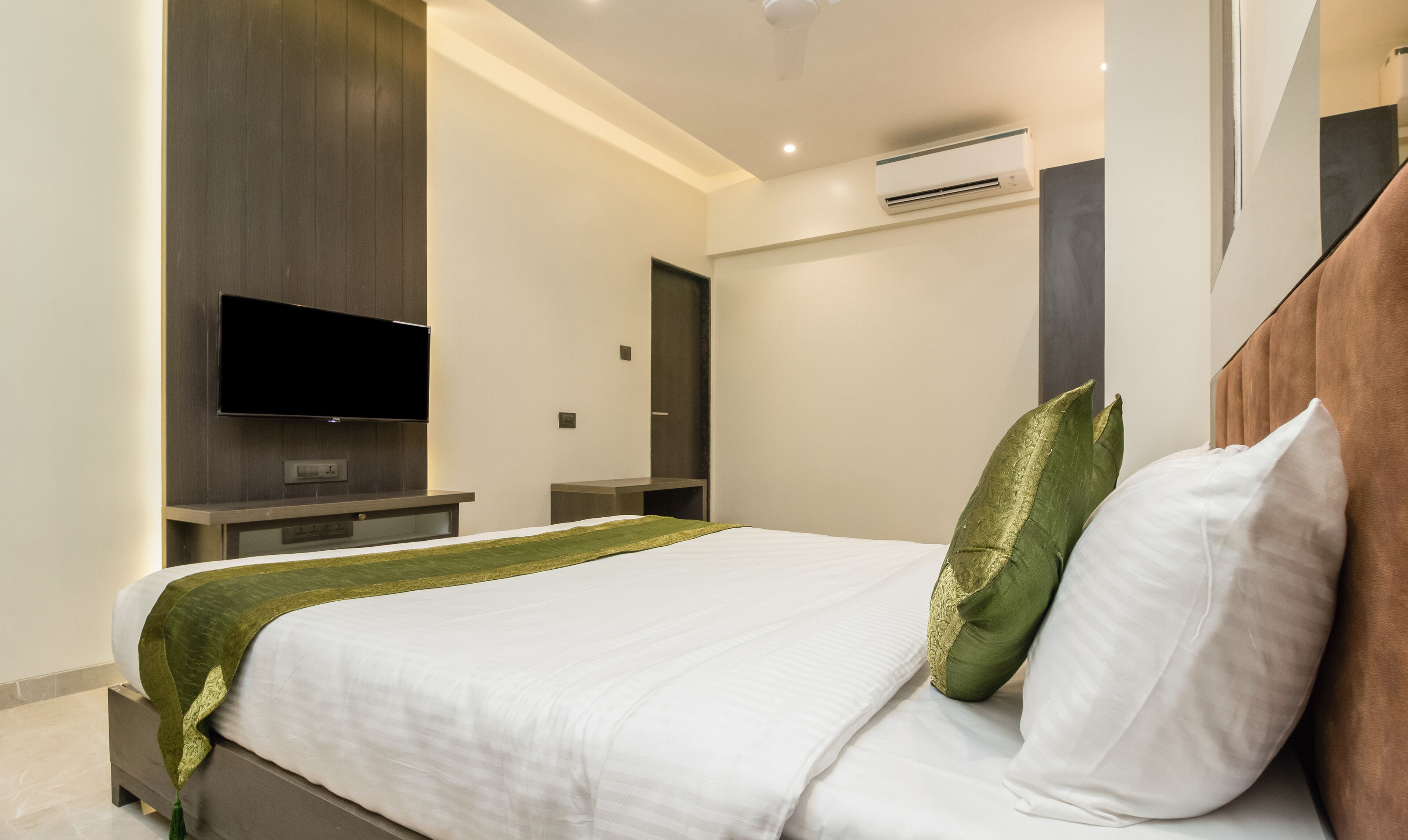 Ein modernes Hotelzimmer mit einem großen Bett, einem flachbildfernseher an der Wand und einer fest installierten Klimaanlage.