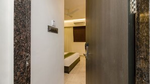 Habitación de hotel con pared de mármol, cama con cubrecama verde, ventilador de techo y aire acondicionado.