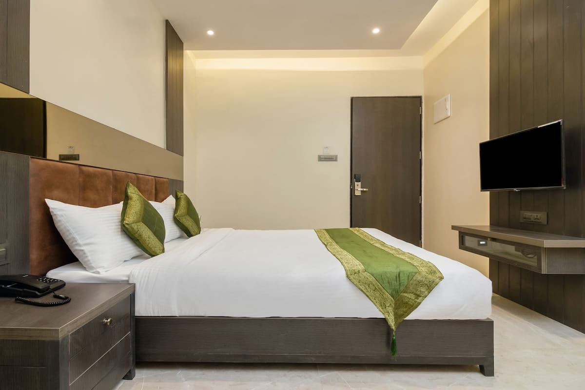 A hotel room with a bed, bedside table, phone, TV, and a mirror.