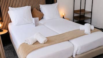 Habitación de hotel con una cama grande, dos mesitas de noche, un estante con perchas en la pared y una obra de arte floral enmarco.