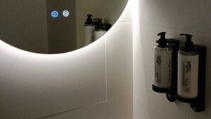 Un baño con un espejo redondo, un lavabo, un grifo, un vaso y dos dispensadores de jabón en la pared.