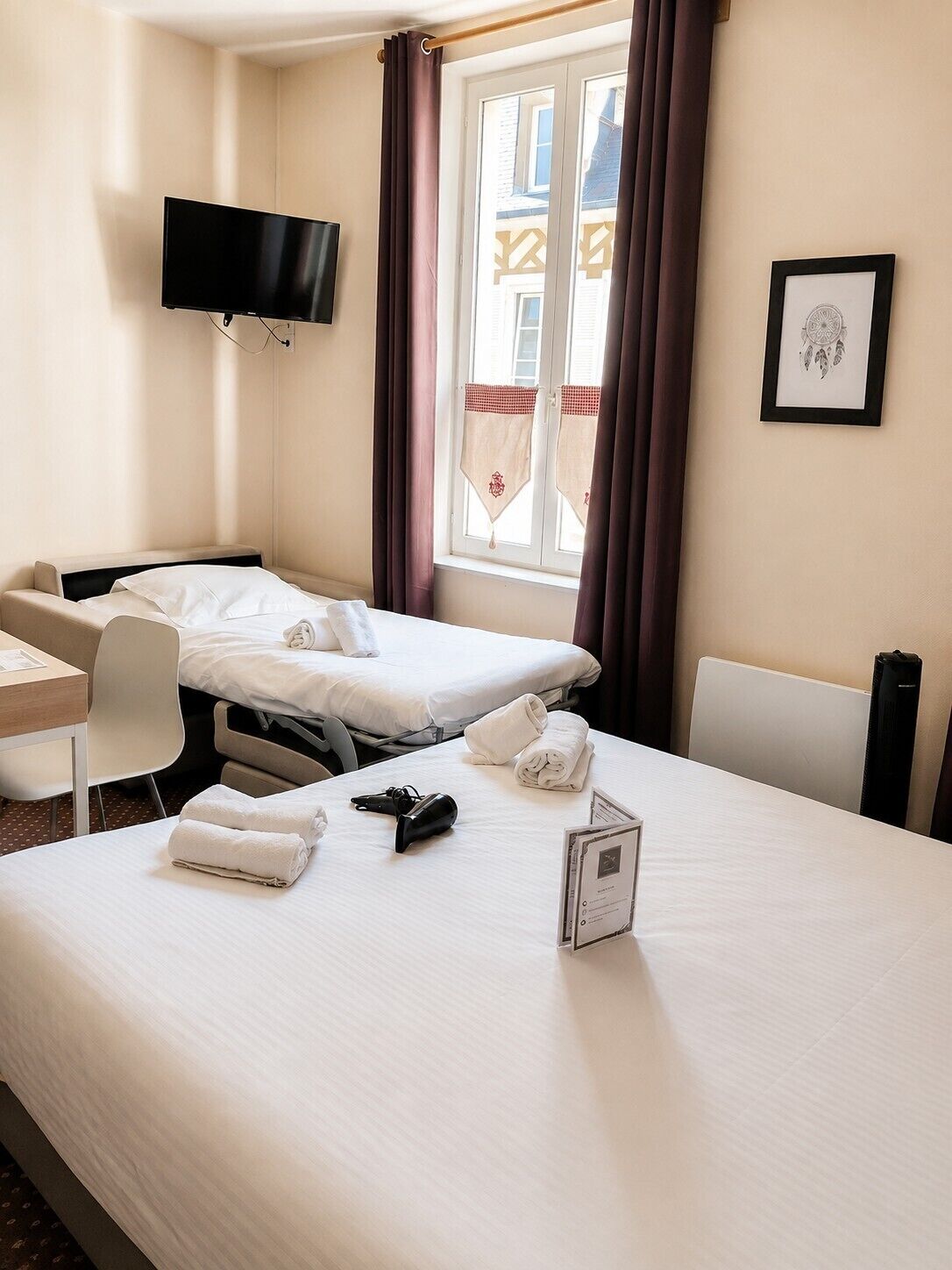 Habitación de hotel con dos camas, un escritorio, una silla, un televisor y una ventana con cortinas.