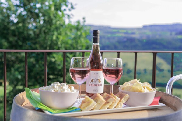 Un plateau avec une bouteille de vin rosé, deux verres, des bols de pop-corn et des chips, le tout posé sur un balcon offrant une vue magnifique.