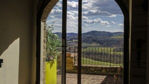 Vista a través de un arco de puerta que da a un balcón con suelo de piedra, con vistas a un paisaje verde y colinas.