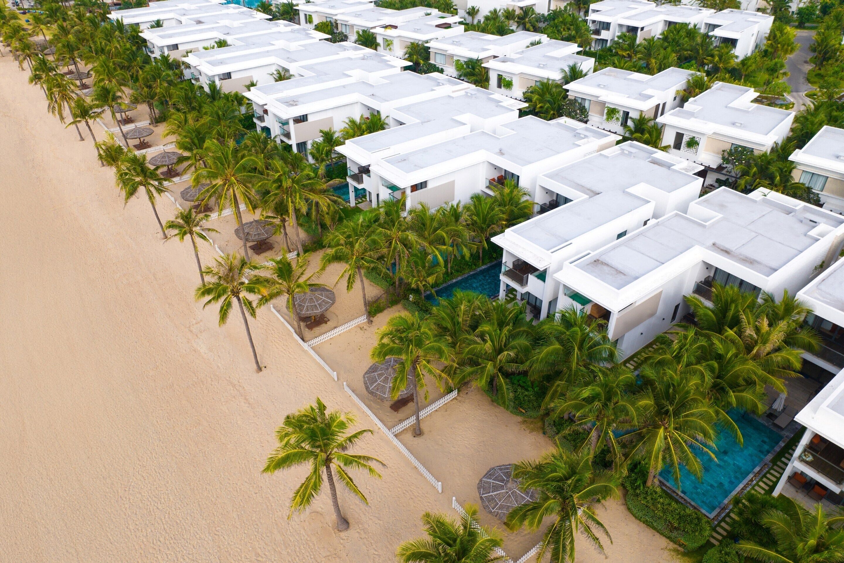A resort with multiple white buildings, a sandy beach, and palm trees.