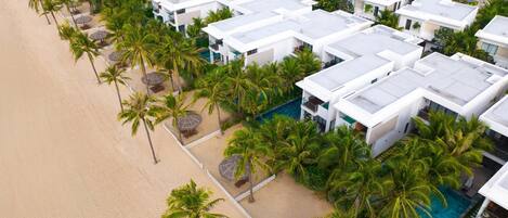 A resort with multiple white buildings, a sandy beach, and palm trees.
