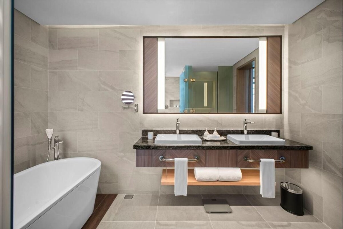 A modern bathroom with two sinks, a large mirror, a bathtub, and a towel rack.