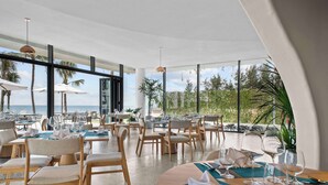 A restaurant with tables set for dining, large windows, and a view of the ocean. - Angsana Ho Tram (Ho Chi Minh City)