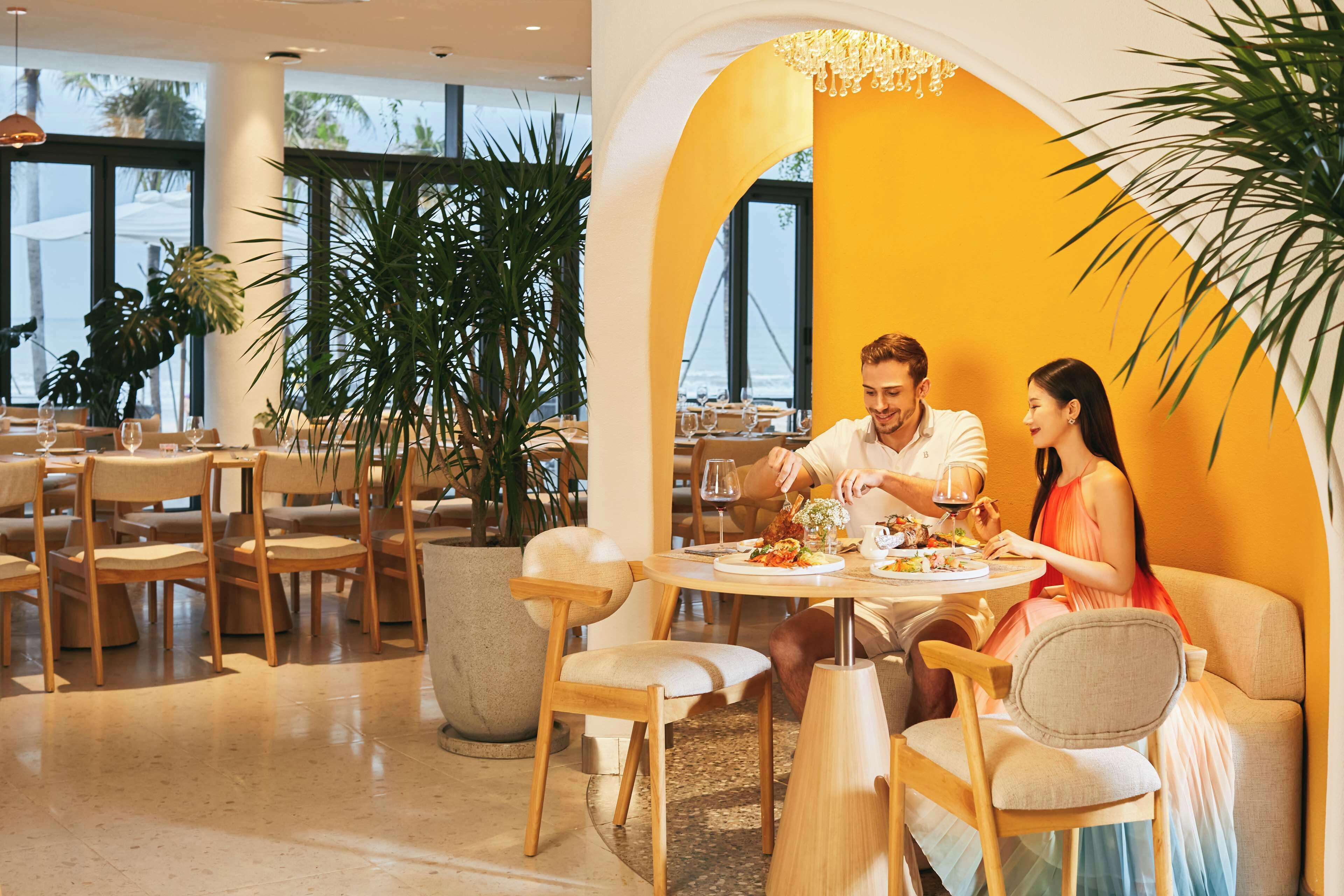Un comedor con mesas redondas, sillas de madera y plantas en macetas.