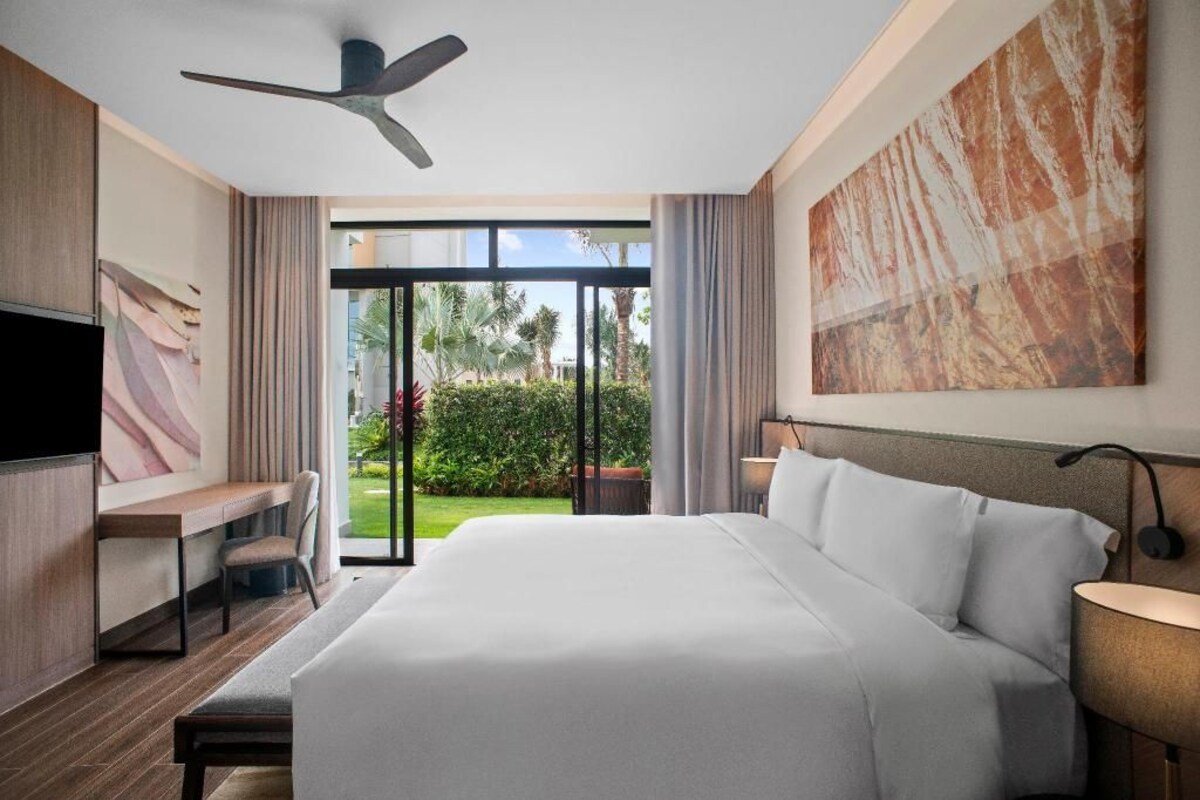 A modern hotel room with a large bed, a desk, a flat-screen TV, and a view of the outdoors.